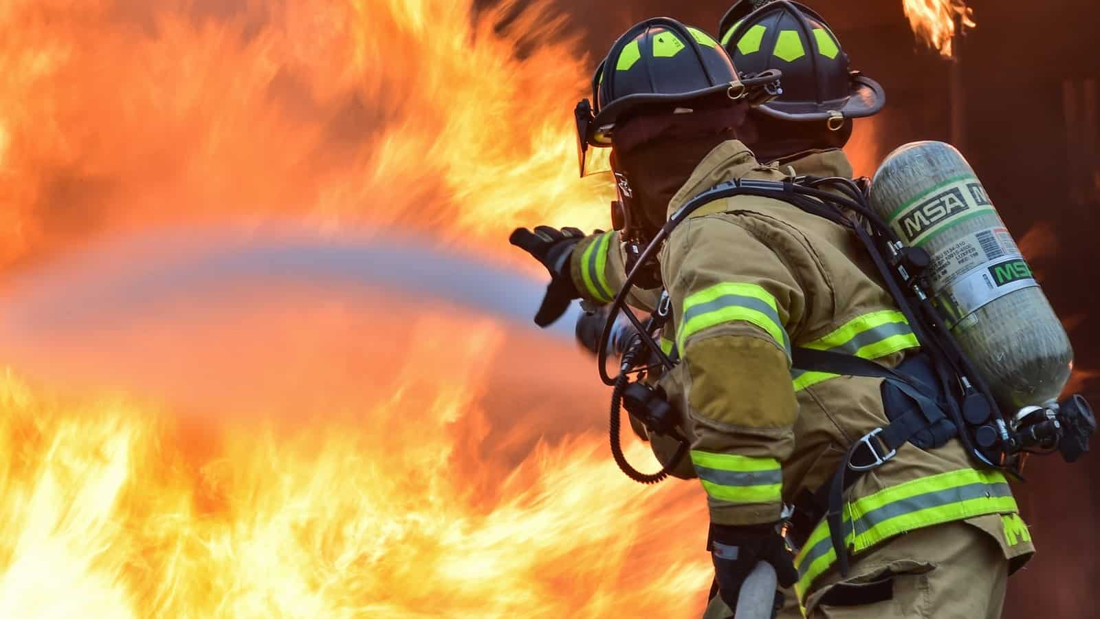 A photo of firemen working a fire hose to extinguish a fire.