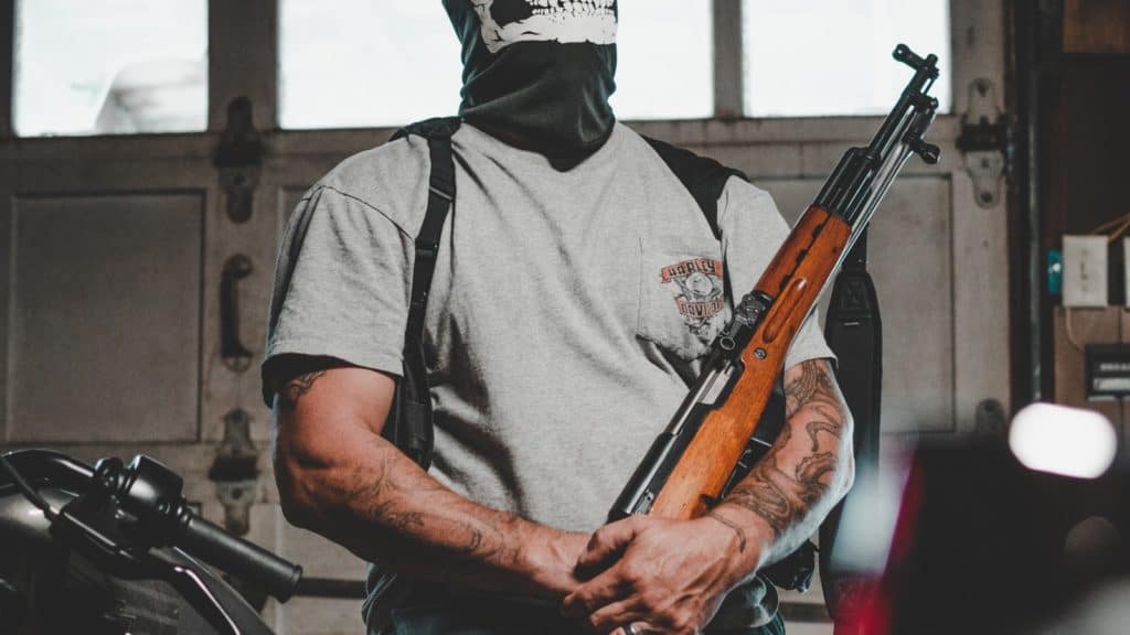 A figure of a masked man with tattoos holding a rifle.