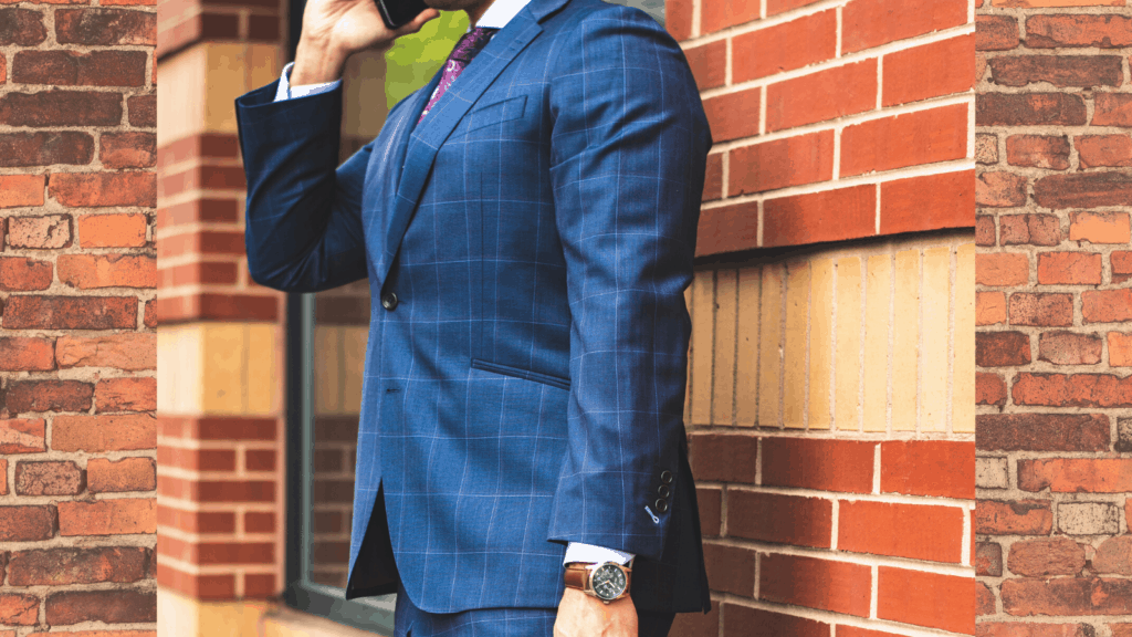 A photo of a man in a suit standing against a brick wall while speaking on a mobile phone.