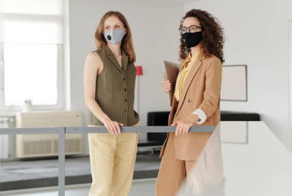 A photo of two masked business women during the Covid-19 pandemic standing at a railing.