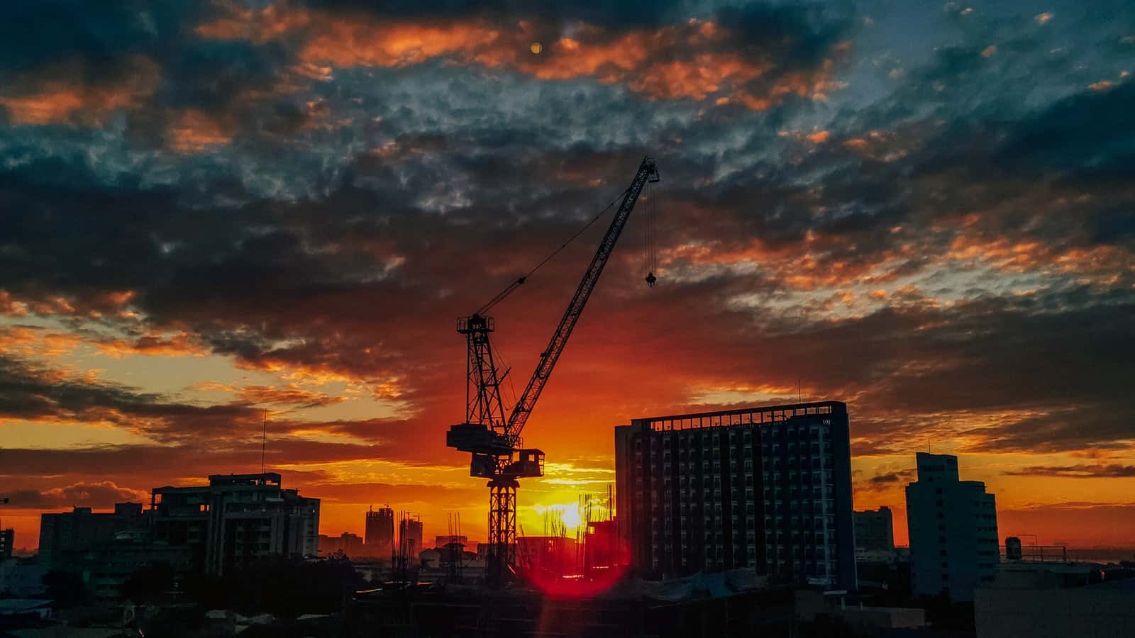 A photo at sunset of city buildings and a construction crane.