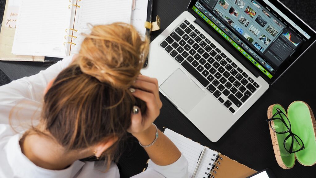 A photo of an employee holding their head while they work at a laptop.