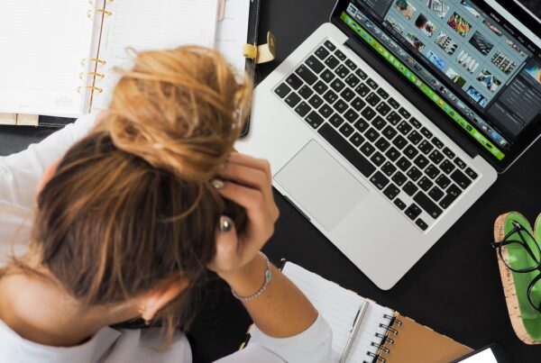 A photo of an employee holding their head while they work at a laptop.