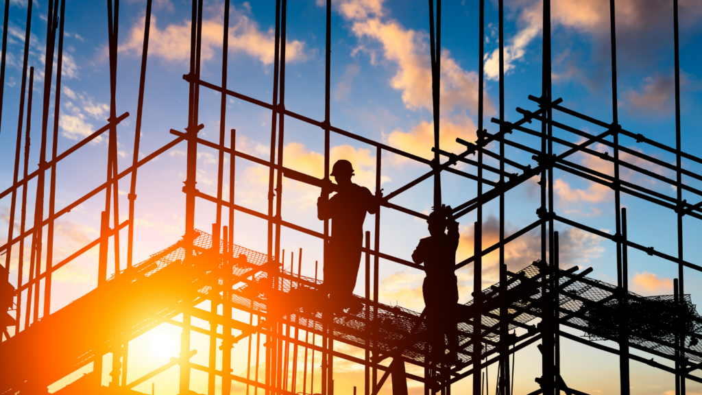 A photo of workers on scaffolding silhouetted by a setting sun.