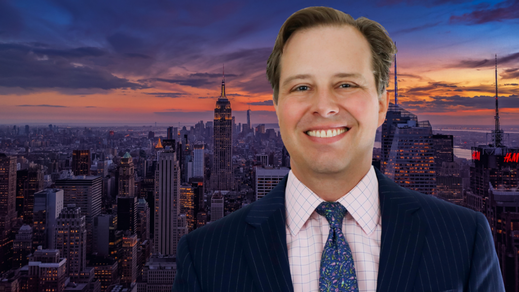 A photo of a Justin Foa with a background of the NYC skyline during sunset.